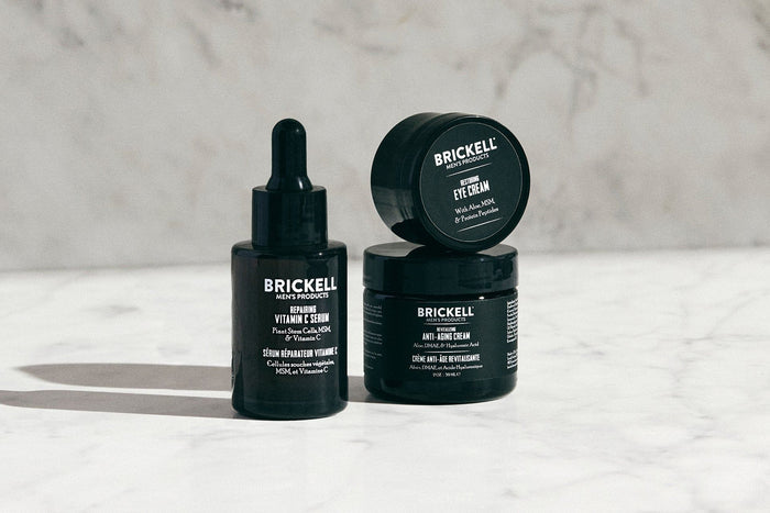 Brickell men's skincare products, including Vitamin C serum, eye cream, and anti-aging cream, on a marble surface.