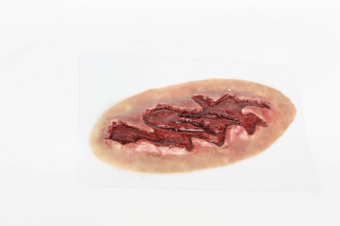 A simulated wound, appearing lacerated and bloody, rests on a white surface.