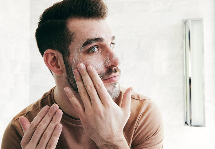 Man applying face cream in a well-lit bathroom.