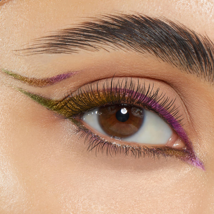 ColourPop Chrome Crème Gel Liner in Chrome Hearted sweeps a metallic multichrome double wing on a brown eye, shifting olive-gold and violet along the upper and lower lash lines with a floating crease accent, shown in a sharp macro close-up.
