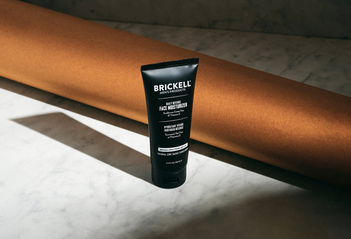 Brickell Men's Daily Defense Face Moisturizer with SPF 20 and natural zinc-based sunscreen on marble surface with brown background roll