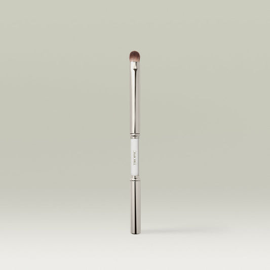 A sleek dual-ended metallic eye makeup brush shown upright with both ends capped, featuring a white center section printed with the brand name.