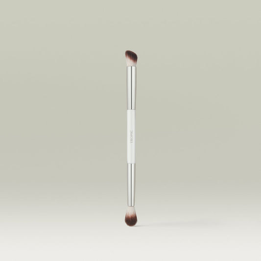 A dual-ended makeup brush with soft, tapered bristles on each end and a sleek white and silver handle, standing upright against a soft neutral background.