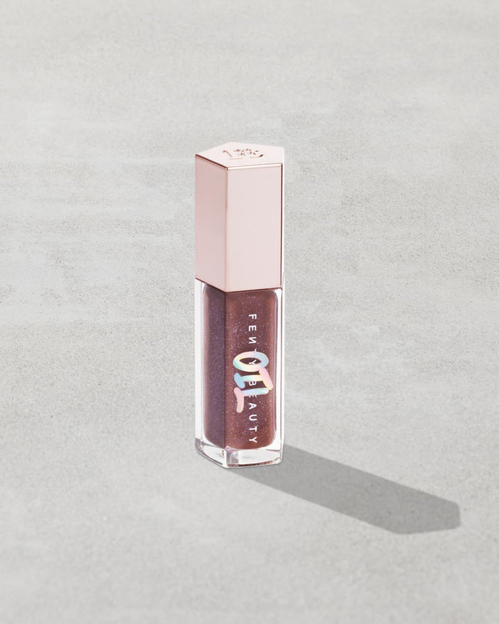 Gloss Bomb Oil Luminizing Oil and  Gloss in shade Rose Amber product against a concrete background.