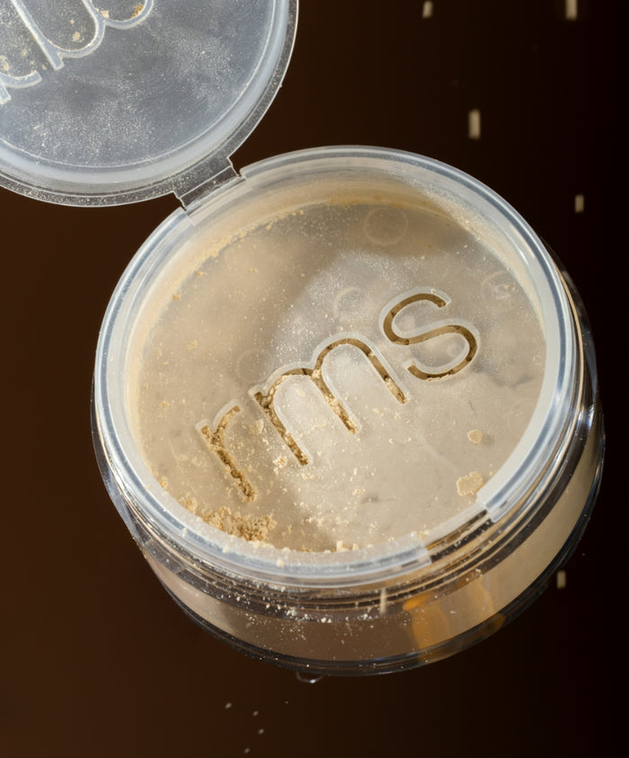 Open container of Hydra Setting Powder with translucent loose powder and RMS Beauty logo on sifter, displayed against dark background, highlighting clean beauty and natural ingredients.