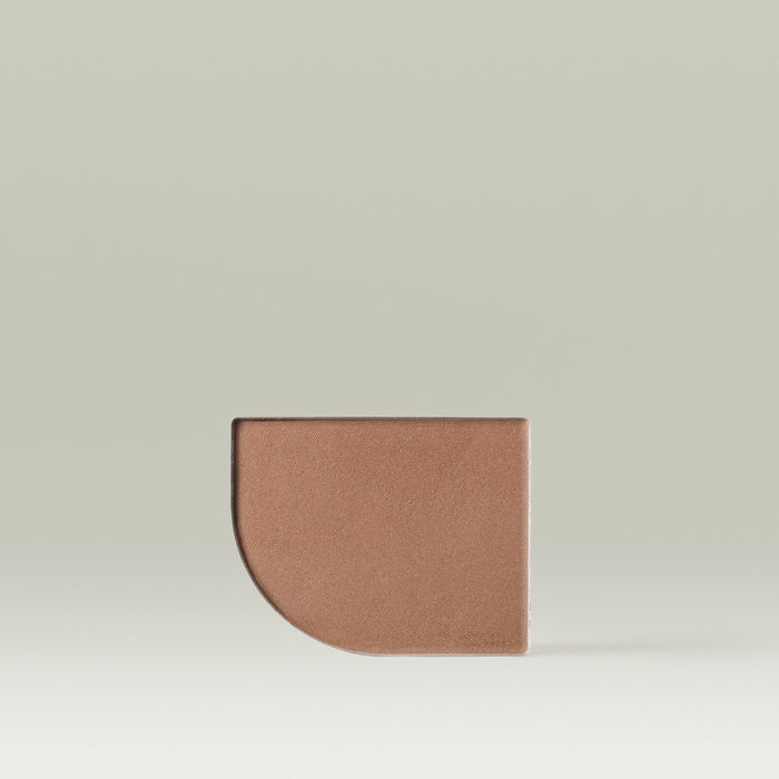 A Tropic Jet Set bronzer refill pan in the shade Tahiti Tan, shown as a large half-moon–shaped pressed powder pan in a warm medium-tan shade against a soft neutral background.