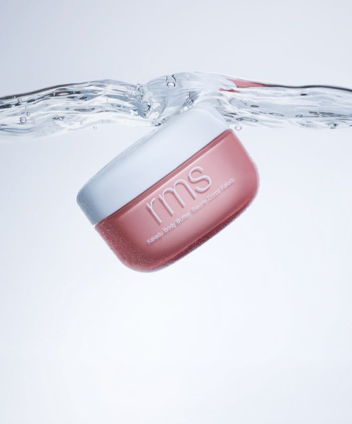Kakadu Body Butter by RMS Beauty in a pink container floating in clear water, emphasizing clean ingredients and hydration in natural body care.