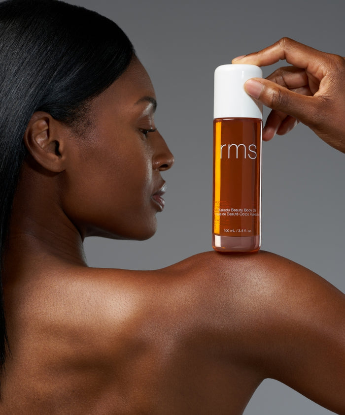 A close-up of a person holding a bottle of Kakadu Body Oil near their shoulder, showcasing smooth, glowing skin and highlighting natural body care with clean, sustainable ingredients.