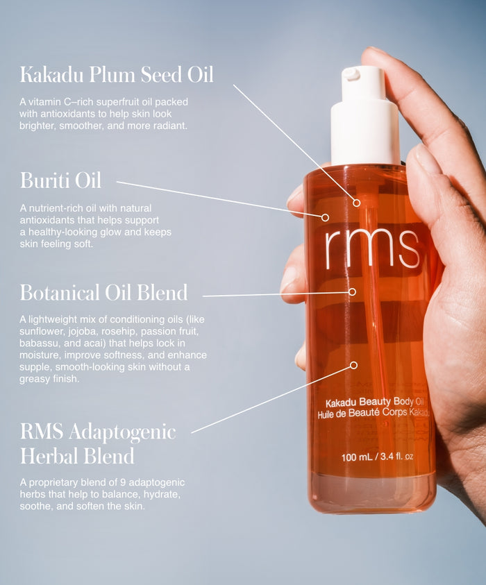 Hand holding a clear pump bottle of Kakadu Body Oil with labels highlighting ingredients including Kakadu Plum Seed Oil, Buriti Oil, Botanical Oil Blend, and RMS Adaptogenic Herbal Blend against a light blue background.