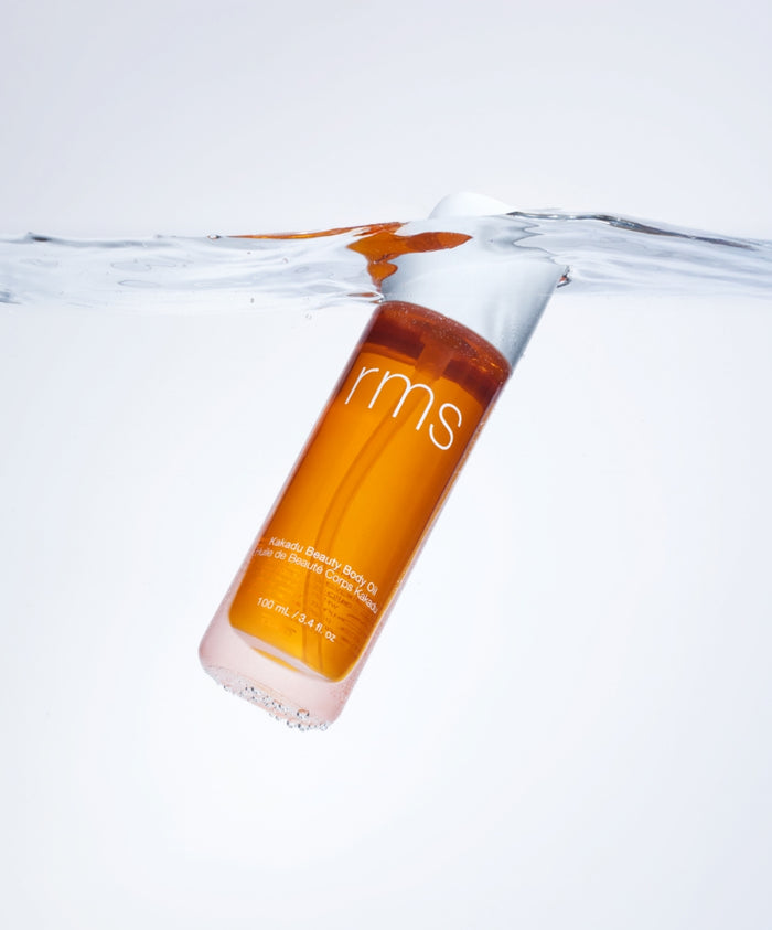 Kakadu Body Oil bottle partially submerged in clear water, showcasing its amber color and sleek design, representing clean beauty and natural ingredient skincare.