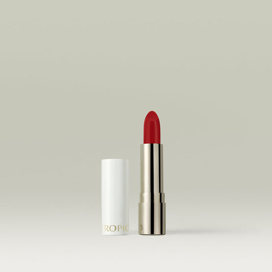 A vibrant red lipstick in a metallic silver tube, shown open with its white cap placed beside it against a soft, neutral background.