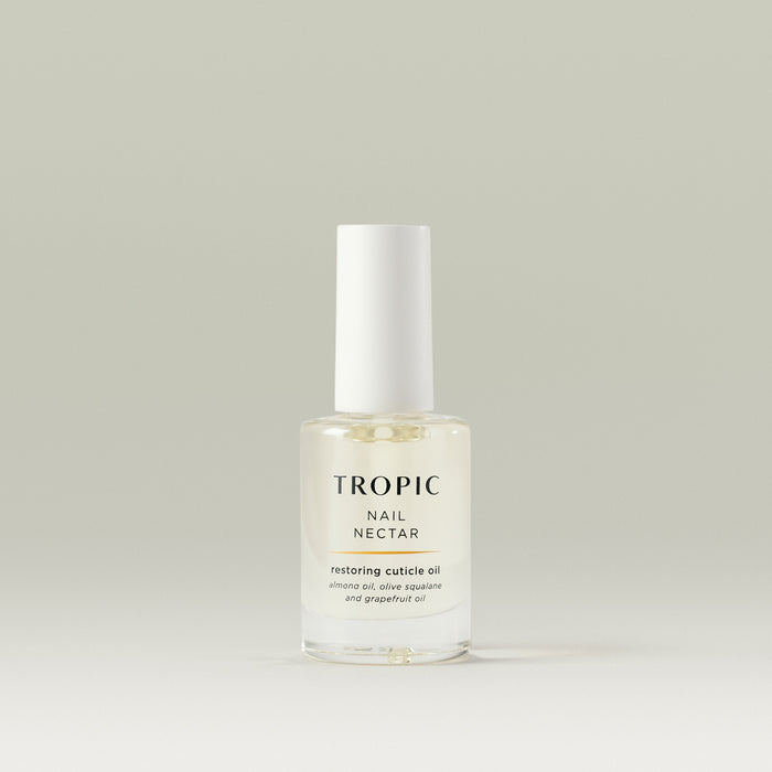 Transparent glass bottle of Tropic Nail Nectar restoring cuticle oil with a white cap, containing almond oil, olive squalane, and grapefruit oil, displayed on a neutral background.