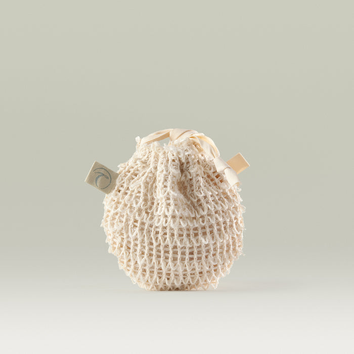Natural cotton mesh pebble pouch with a drawstring closure and Tropic tag, designed for storing and using cleansing pebbles.