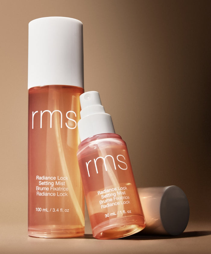 Two translucent bottles of Radiance Lock Setting Mist with white caps, shown against a warm brown background highlighting the skincare infused makeup product from RMS Beauty.