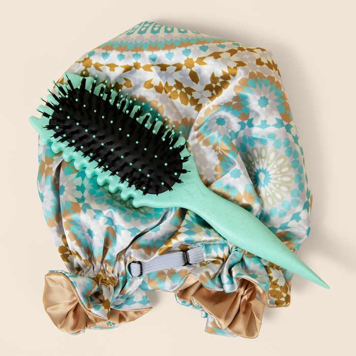 A teal Bounce Curl brush sits on top of a satin bonnet
